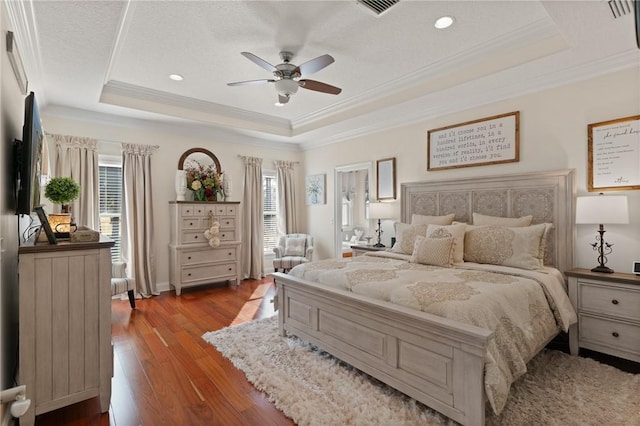 bedroom with crown molding, light wood-type flooring, ceiling fan, and a tray ceiling