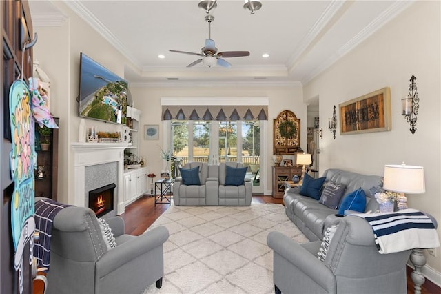 living room featuring ceiling fan, ornamental molding, a raised ceiling, and light hardwood / wood-style flooring