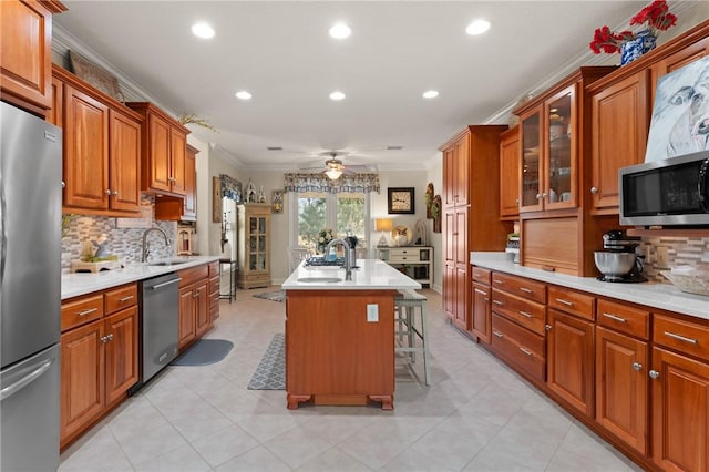 kitchen with a breakfast bar, backsplash, stainless steel appliances, ornamental molding, and a center island with sink