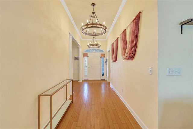 corridor featuring light wood finished floors, baseboards, crown molding, and an inviting chandelier