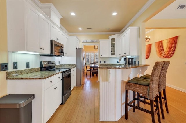 kitchen with visible vents, glass insert cabinets, a breakfast bar, a peninsula, and stainless steel appliances