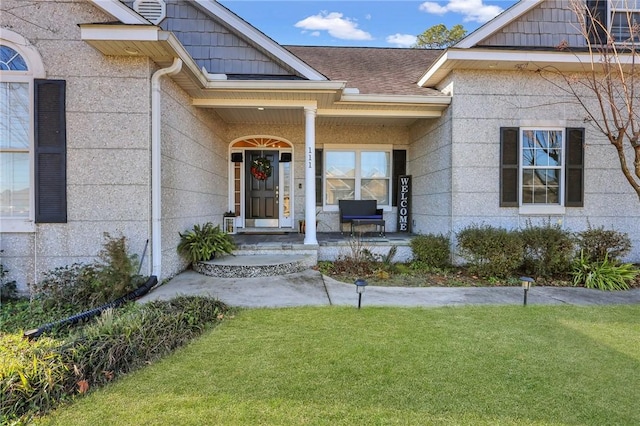 doorway to property with a lawn, covered porch, and roof with shingles