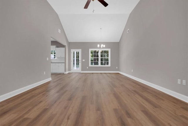 unfurnished living room featuring wood-type flooring, ceiling fan with notable chandelier, and high vaulted ceiling