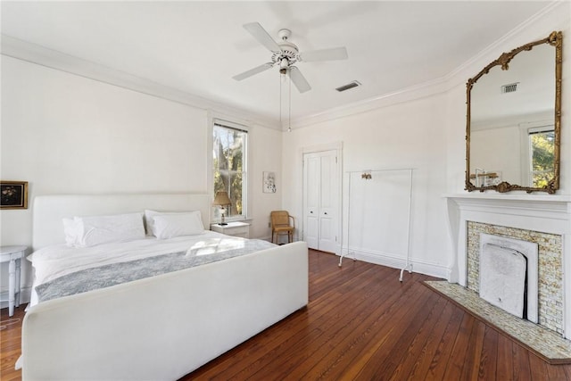 bedroom featuring a closet, ornamental molding, dark wood-type flooring, a premium fireplace, and ceiling fan