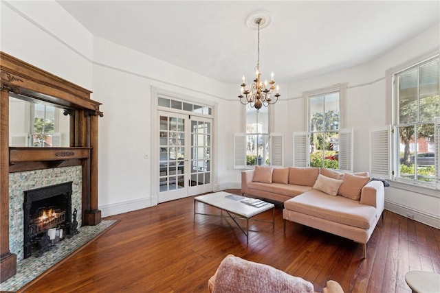 living room with a notable chandelier, french doors, a stone fireplace, and dark wood-type flooring