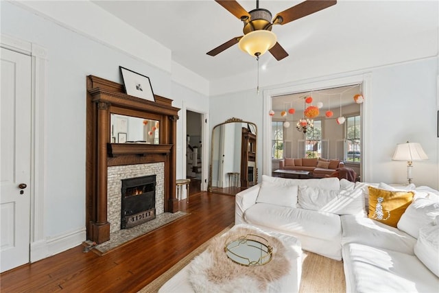 living room featuring wood-type flooring, ceiling fan, and a stone fireplace