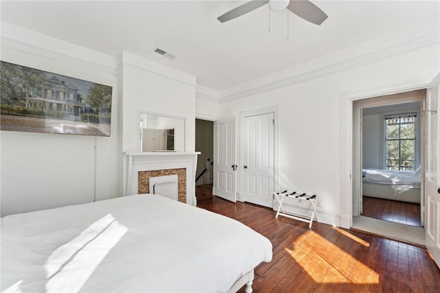 bedroom featuring a fireplace, a closet, ornamental molding, dark hardwood / wood-style flooring, and ceiling fan