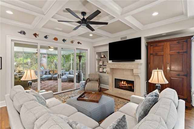 living room featuring light hardwood / wood-style flooring, coffered ceiling, a tiled fireplace, built in shelves, and beamed ceiling