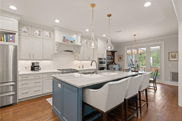 kitchen featuring sink, hanging light fixtures, appliances with stainless steel finishes, an island with sink, and white cabinets