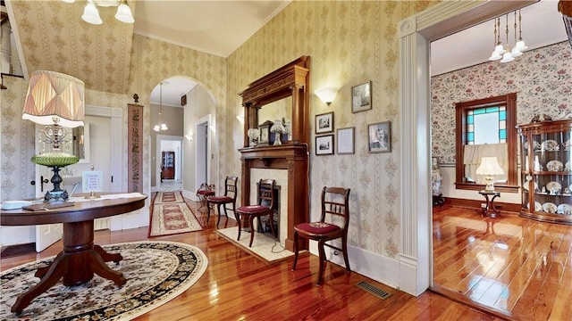 foyer entrance featuring a fireplace, baseboards, arched walkways, wallpapered walls, and hardwood / wood-style flooring