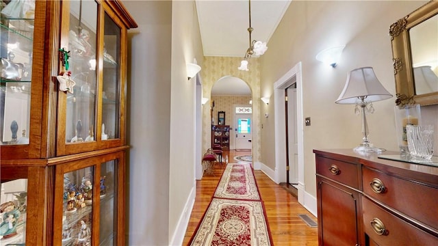 corridor with light wood finished floors, visible vents, baseboards, arched walkways, and wallpapered walls
