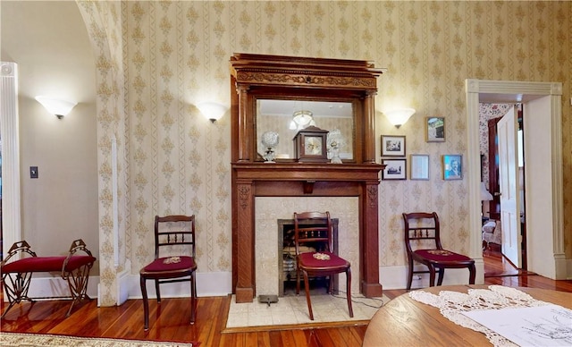sitting room with a fireplace, baseboards, wallpapered walls, and wood-type flooring