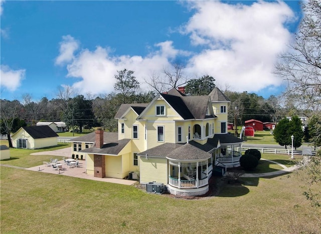 view of property exterior with a patio, an outbuilding, roof with shingles, a lawn, and fence