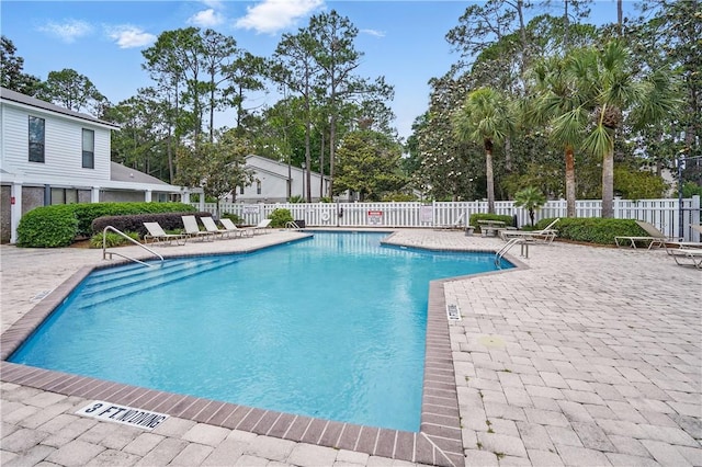 community pool featuring fence, a patio area, and view of wooded area