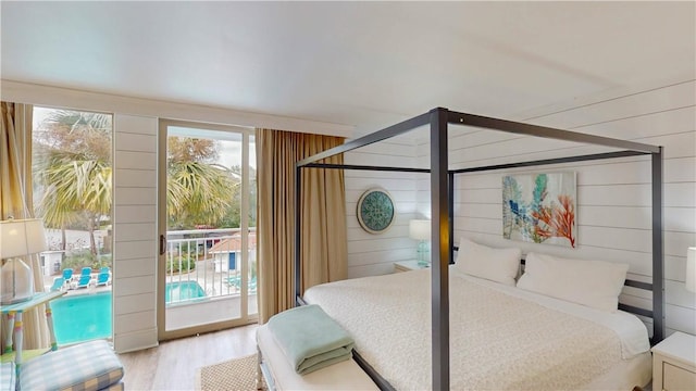 bedroom featuring access to outside, light hardwood / wood-style floors, and wood walls