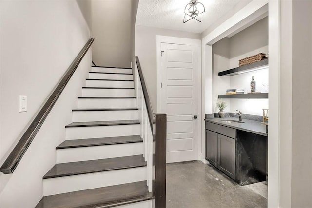 stairs with concrete flooring, a textured ceiling, and indoor wet bar