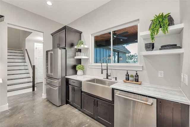 kitchen with dark brown cabinetry, light stone counters, sink, and stainless steel appliances