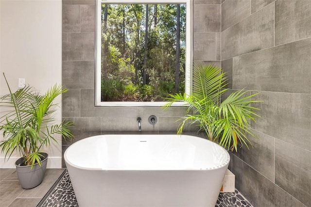 bathroom with a bathing tub, a wealth of natural light, and tile walls