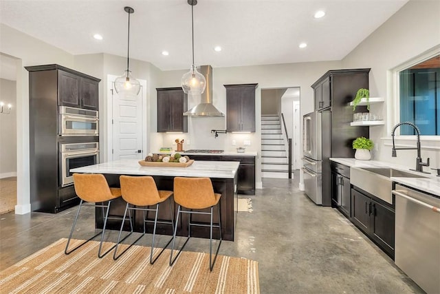 kitchen with dark brown cabinetry, wall chimney range hood, hanging light fixtures, and appliances with stainless steel finishes