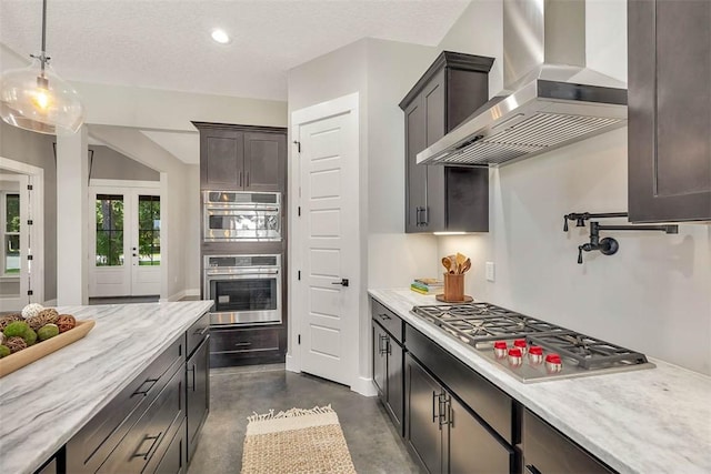 kitchen with wall chimney exhaust hood, a textured ceiling, stainless steel appliances, dark brown cabinetry, and hanging light fixtures