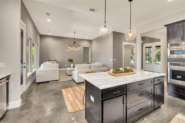 kitchen with light stone counters, concrete flooring, stainless steel appliances, a kitchen island, and hanging light fixtures