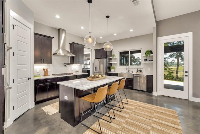 kitchen featuring wall chimney exhaust hood, concrete floors, a breakfast bar, a kitchen island, and appliances with stainless steel finishes