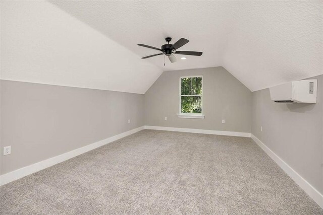 additional living space with ceiling fan, a wall mounted air conditioner, vaulted ceiling, a textured ceiling, and carpet