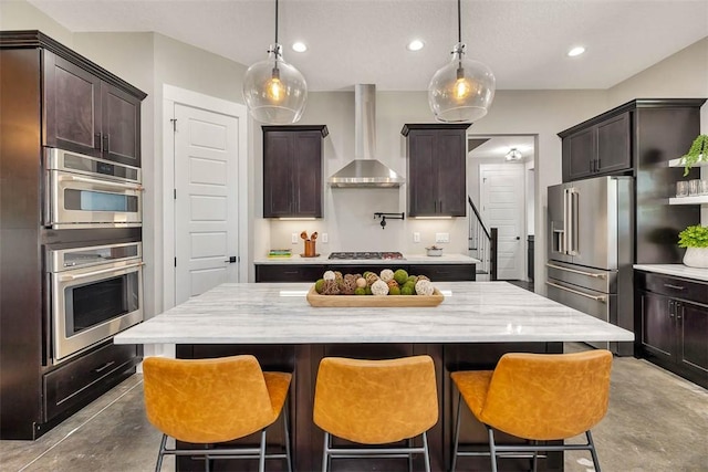 kitchen featuring appliances with stainless steel finishes, a kitchen island, dark brown cabinets, and wall chimney exhaust hood