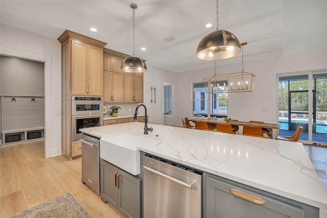 kitchen with light stone counters, light wood-type flooring, decorative light fixtures, and appliances with stainless steel finishes