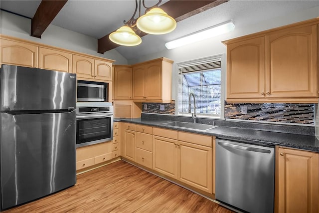 kitchen featuring decorative light fixtures, dark countertops, light brown cabinetry, appliances with stainless steel finishes, and a sink