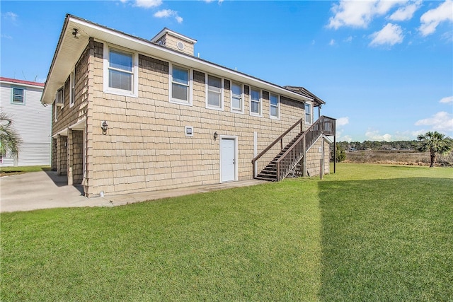 rear view of property featuring a lawn and stairs