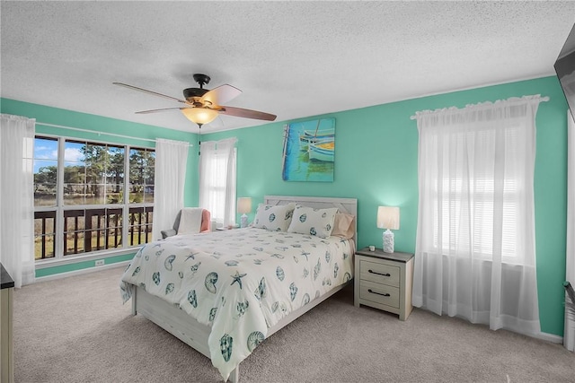 bedroom featuring a ceiling fan, light colored carpet, multiple windows, and a textured ceiling