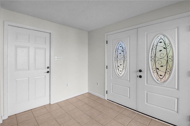 foyer featuring a textured ceiling, baseboards, and light tile patterned floors