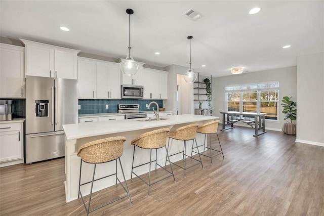 kitchen with hanging light fixtures, an island with sink, appliances with stainless steel finishes, and white cabinets