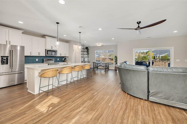 kitchen with stainless steel appliances, pendant lighting, a center island with sink, and white cabinets