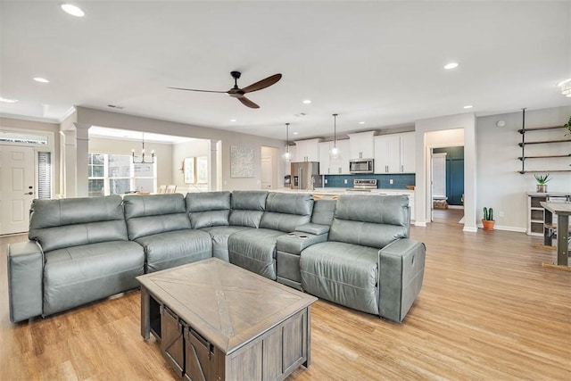 living room with ceiling fan with notable chandelier, light wood-type flooring, and ornate columns