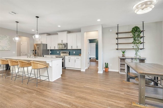 kitchen with white cabinetry, backsplash, a kitchen island with sink, light hardwood / wood-style floors, and stainless steel appliances