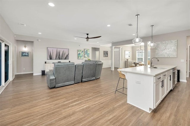 kitchen with sink, white cabinetry, a kitchen island with sink, hanging light fixtures, and light hardwood / wood-style floors