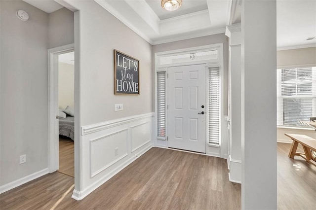 entrance foyer with ornamental molding, light wood-type flooring, and a tray ceiling