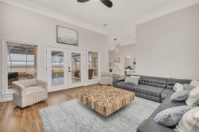 living room with ceiling fan, hardwood / wood-style floors, a towering ceiling, ornamental molding, and french doors