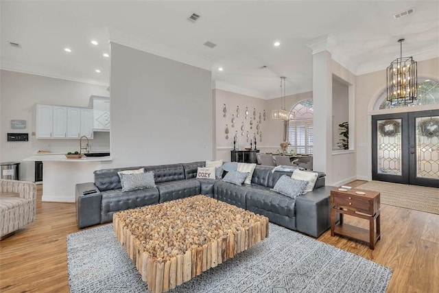 living room featuring an inviting chandelier, sink, ornamental molding, light wood-type flooring, and french doors