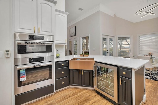 kitchen featuring sink, white cabinetry, double oven, kitchen peninsula, and beverage cooler