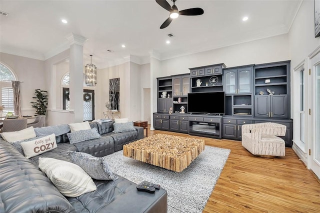 living room featuring ceiling fan with notable chandelier, crown molding, light hardwood / wood-style floors, and decorative columns