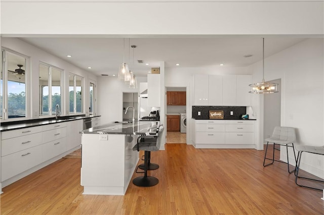 kitchen featuring white cabinets, a large island with sink, a kitchen bar, and washer / clothes dryer