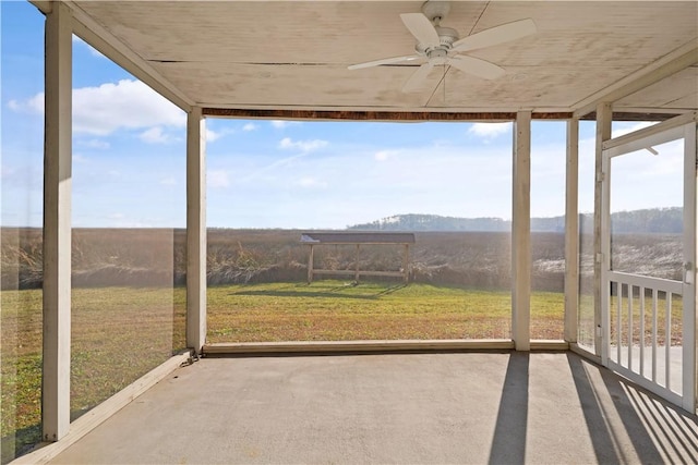 unfurnished sunroom with ceiling fan and a rural view