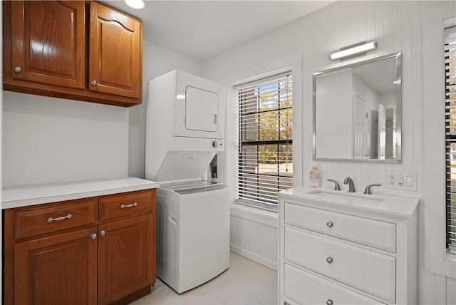 washroom with cabinets, light tile patterned floors, stacked washer and dryer, and sink