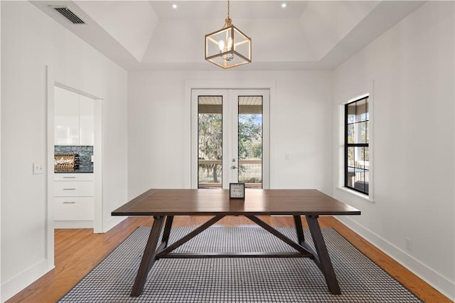 dining area featuring french doors, light wood-type flooring, a raised ceiling, and a notable chandelier