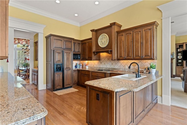 kitchen featuring light wood finished floors, tasteful backsplash, a sink, light stone countertops, and a peninsula