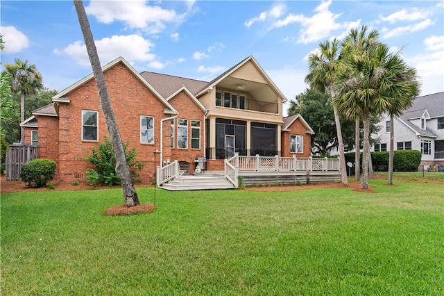 back of house with a deck, brick siding, a lawn, and a sunroom