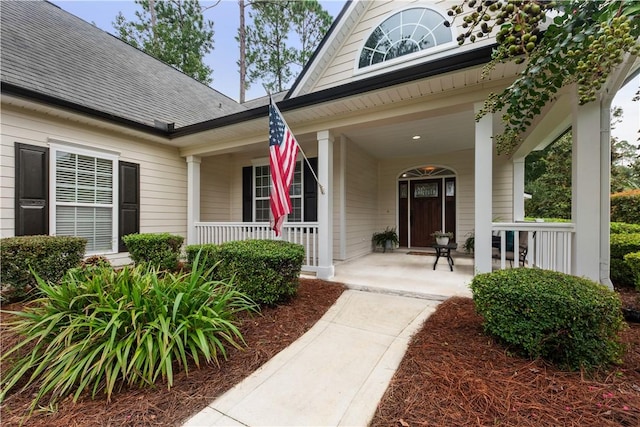 view of exterior entry featuring a shingled roof and a porch